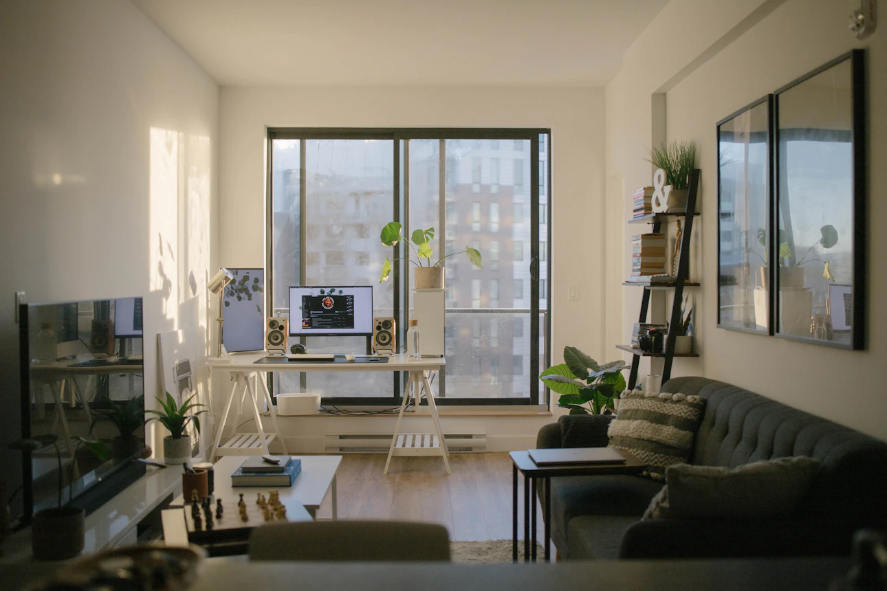 A small, sunlit apartment living room with a city view through large windows, representing space-conscious urban prepping