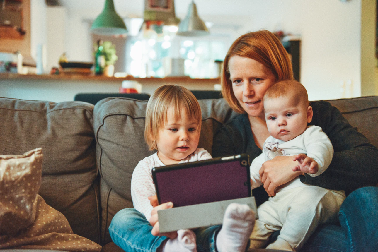 A parent sitting on a couch at home with two young children, representing family and kids emergency preparedness planning