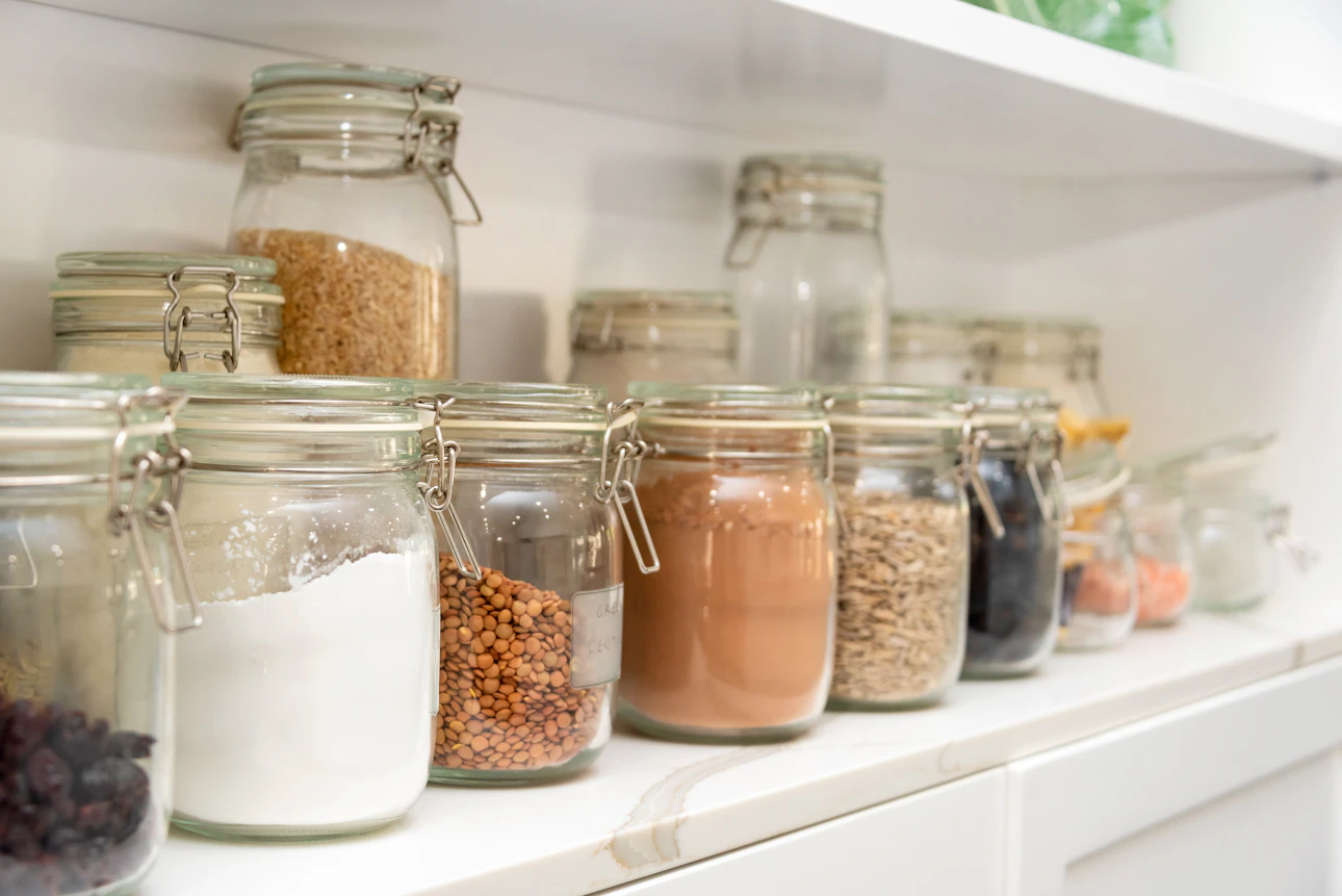 Glass jars of dry pantry staples like grains and beans organized on a shelf, the kind of simple food storage a new prepper starts with