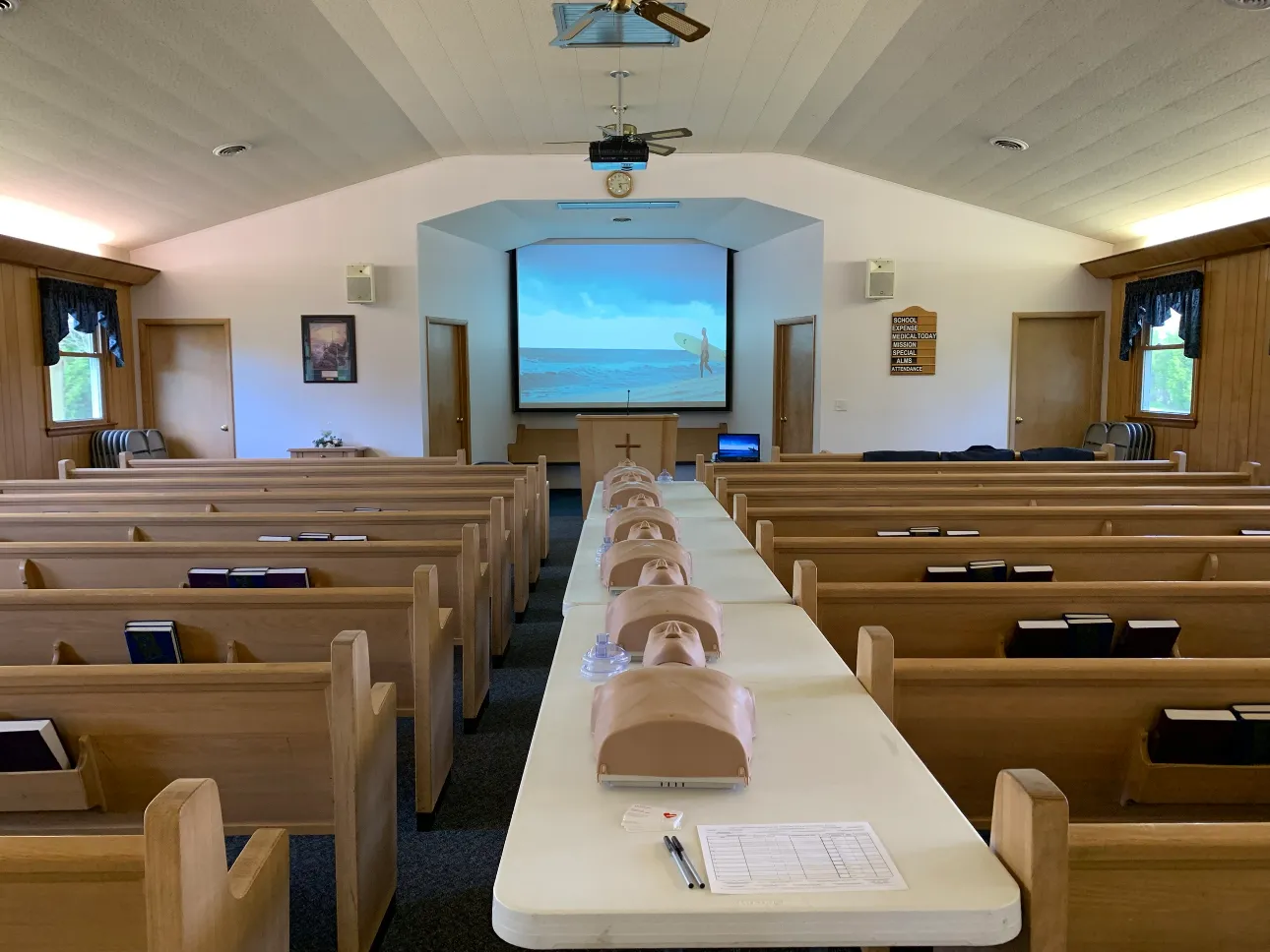Church classroom set up for a CPR class, with a row of adult CPR training manikins and face shields on tables between the pews